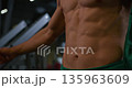 Close-up showcases muscular torso of adult man in gym, highlighting defined abs and physique. Demonstrates dedication to fitness and bodybuilding, emphasizing strength and health indoors. 135963609