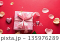 A pink gift box spins as the camera orbits, satin bow shining amid petals and hearts on crimson 135976289