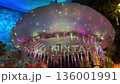 A giant jellyfish light sculpture glows with pink and white dots across its smooth dome. Long translucent tentacles hang down in an immersive underwater themed room. 136001991