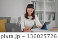 自宅のリビングでノートパソコンを使いながら笑顔で見つめる、ブラウス姿の若手日本人女性。在宅ワーク・ラ 136025726