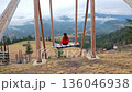 Woman in red sweater on wooden swing, female looking at mountain valley view 136046938