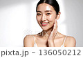 This is a portrait of a woman touching her moist, smooth skin in a brightly lit studio. 136050212