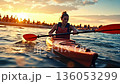 A woman paddling a kayak in the ocean at sunset 136053299
