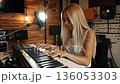 A woman playing a keyboard in front of a microphone 136053303