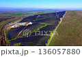 Elevated wide-angle view of an expansive solar energy complex. Includes rows of photovoltaic panels, a central electrical substation, and a service road leading through the hills. 136057880