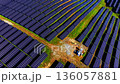 Section of a solar farm with a transformer or inverter unit on a patch of earth. Rows of blue solar panels surround the equipment on a green field. 136057881