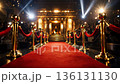 Elegant woman in black dress walks down red carpet towards grand entrance, surrounded by photographers and bright lights in a glamorous event setting 136131130