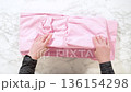 A pair of hands smooths and folds a soft pink fabric on a light surface. The material appears lightweight and neatly arranged. The scene is bright and minimal with clean, even lighting. 136154298