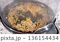 Yellow corn kernels sit evenly in a hot popcorn maker before popping begins. The view shows the black base and clear lid with a thin layer of steam starting to form. 136154434