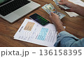 Senior entrepreneur organizes stack of dollar bills counting financial invoices on phone, focused man prepares to make payments for utility bills using cash slow motion 136158395