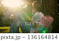 Child girl relaxing with book in nature park. Education. School Girl sitting with book under tree on lawn park. Training. Teenage schoolgirl with school backpack reads textbook while sitting city park 136164814