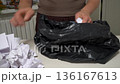 Man folds crumpled white papers into a black trash bag 136167613