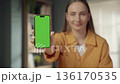 Woman holding a smartphone with a blank green screen display, allowing for the easy insertion of custom content, app interfaces, or promotional material to showcase digital concepts and technology 136170535