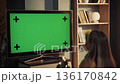 Woman enjoying a beverage while watching a television with a green screen and tracking markers, providing a customizable mockup for content display in a home interior setting 136170842