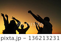People dance at music concert, raising their hands in air. Dancing party, group happy people raising their hands to sky in evening. People having fun outdoors, dancing on beach, relaxing in nature. 136213231