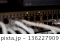 Server room rack with network cables. Network cables connect to server rack ports with blurry bokeh lights in the background. A close-up of a network rack with multiple Ethernet cables connected to it 136227909