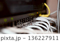 Server room rack with network cables. Network cables connect to server rack ports with blurry bokeh lights in the background. A close-up of a network rack with multiple Ethernet cables connected to it 136227911