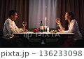 Couple have romantic candlelit dinner home, enjoying wine glasses and conversation. Date love night, anniversary celebration, casual evening gathering. Cozy candle light. Man and woman enjoy talking. 136233098