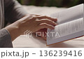 Close-up, woman reading a book and turning a page while sitting at a table in a room 136239416