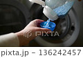 Hand pouring blue detergent powder pills in blue plastic cap, scoop near to washing machine. Lifestyle video, natural light 136242457