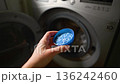 Hand holding blue detergent powder pills in blue plastic cap, scoop near to washing machine. Lifestyle video, natural light 136242460