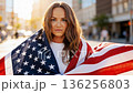 Camera moving to low angle view. Proud serious young woman standing on street holding usa flag under blue sky looking at camera. 136256803