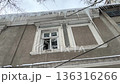 Low angle view of an old residential building with dangerous long icicles hanging from the roof edge above windows, posing a threat to pedestrians during a cold and frosty winter day 136316266