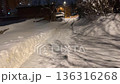 First person perspective of walking along a narrow, snowy urban path in the evening, surrounded by deep snowdrifts and illuminated by streetlights that cast long, dark shadows from the trees 136316268