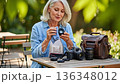 Senior European Woman Photographer Cleaning Camera Lens at Outdoor Park Table with Professional Photography Equipment 136348012
