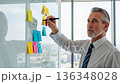Senior European businessman writing on colorful sticky notes during office brainstorming session and strategic planning meeting 136348028