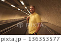 Man in yellow shirt standing on moving walkway in underground tunnel 136353577
