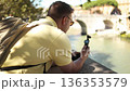 Tourist filming historic bridge and river with action camera in European city 136353579