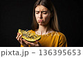 Woman examines yellow watermelon slice with a confused expression in dark setting 136395653