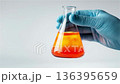Experiment with orange liquid in a flask held by a hand in a laboratory setting during daytime 136395659