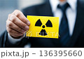 Man holds yellow card with nuclear symbol in office setting during daytime 136395660