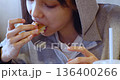 Close-up 4k footage of a Caucasian teenage girl eats a burger in a cafe, enjoying every tasty bite while relaxing in a casual and warm environment. Slow motion video. 136400266