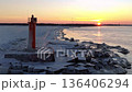 Red lighthouse illuminates icy pier during sunset. Warm sunset casts glow on icy jetty with lighthouse 136406294