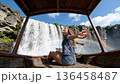 Young girl posing with her back on a waterfall posing. A beautiful woman sits in the thai boat and rises her hand near big waterfalls  136458487