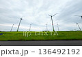 Wind turbines spin in green fields during the day near a rural road under cloudy skies 136492192