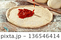 Super slow motion closeup of rich tomato sauce being poured onto freshly shaped pizza dough.  136546414