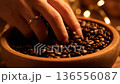 A close-up shot of a hand gently touching fresh, dark roasted coffee beans in a wooden bowl. 136556087