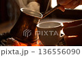 Steaming hot coffee prepared in a traditional copper pot over glowing coals, a classic method. 136556090