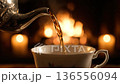 Pouring warm tea into a teacup. Cozy evening with fireplace and candles in background. 136556094