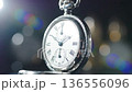 An elegant silver pocket watch featuring Roman numerals, set against a blurred background. 136556096