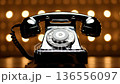 A classic black rotary telephone, with its chrome dial, sits against a warm, blurred bokeh background. 136556097