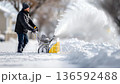 Snow removal process with a snowblower clearing a path after winter storm, showcasing action and movement in a snowy environment 136592488