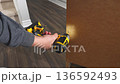 Hand using power drill to secure screws into wooden surface, showcasing the assembly process with tools and focused action in a home setting 136592493