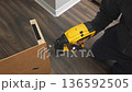 Skilled individual using a power tool to secure wooden panel, showcasing precise action in a well-lit indoor environment, demonstrating craftsmanship 136592505