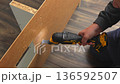 Individual using power tool to cut through wooden board, showcasing precise action and craftsmanship in a well-lit workspace 136592507