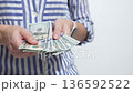 Individual with striped shirt is holding cash in hands, showcasing a financial transaction, camera zooms in on the money being counted 136592522